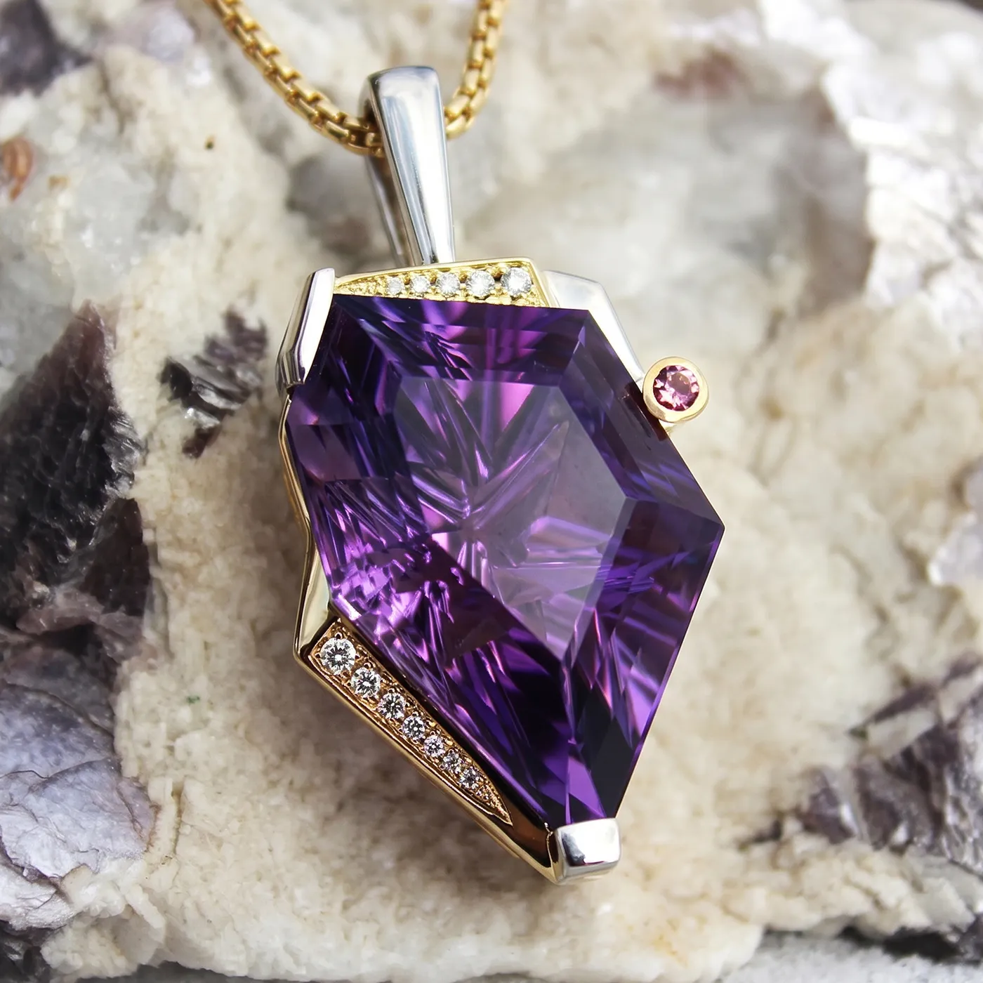 A faceted purple gemstone pendant with gold and diamond accents on a textured background.