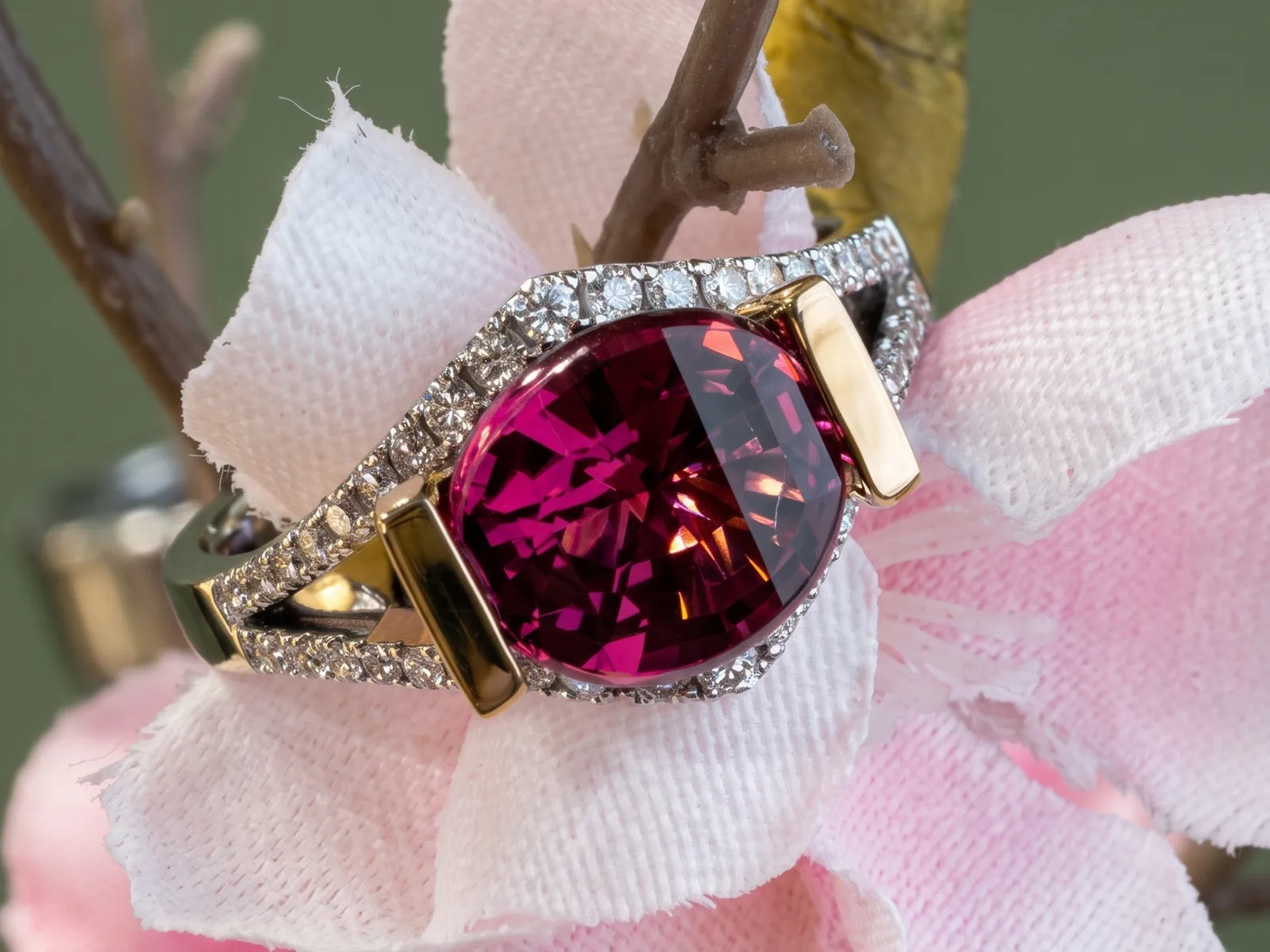 A garnet ring with a large red stone and diamond accents on a pink flower background.