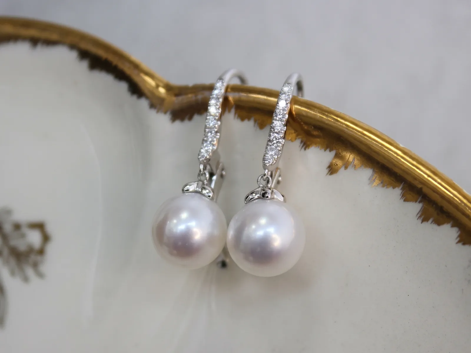 Elegant pearl earrings with diamond accents on a decorative dish.