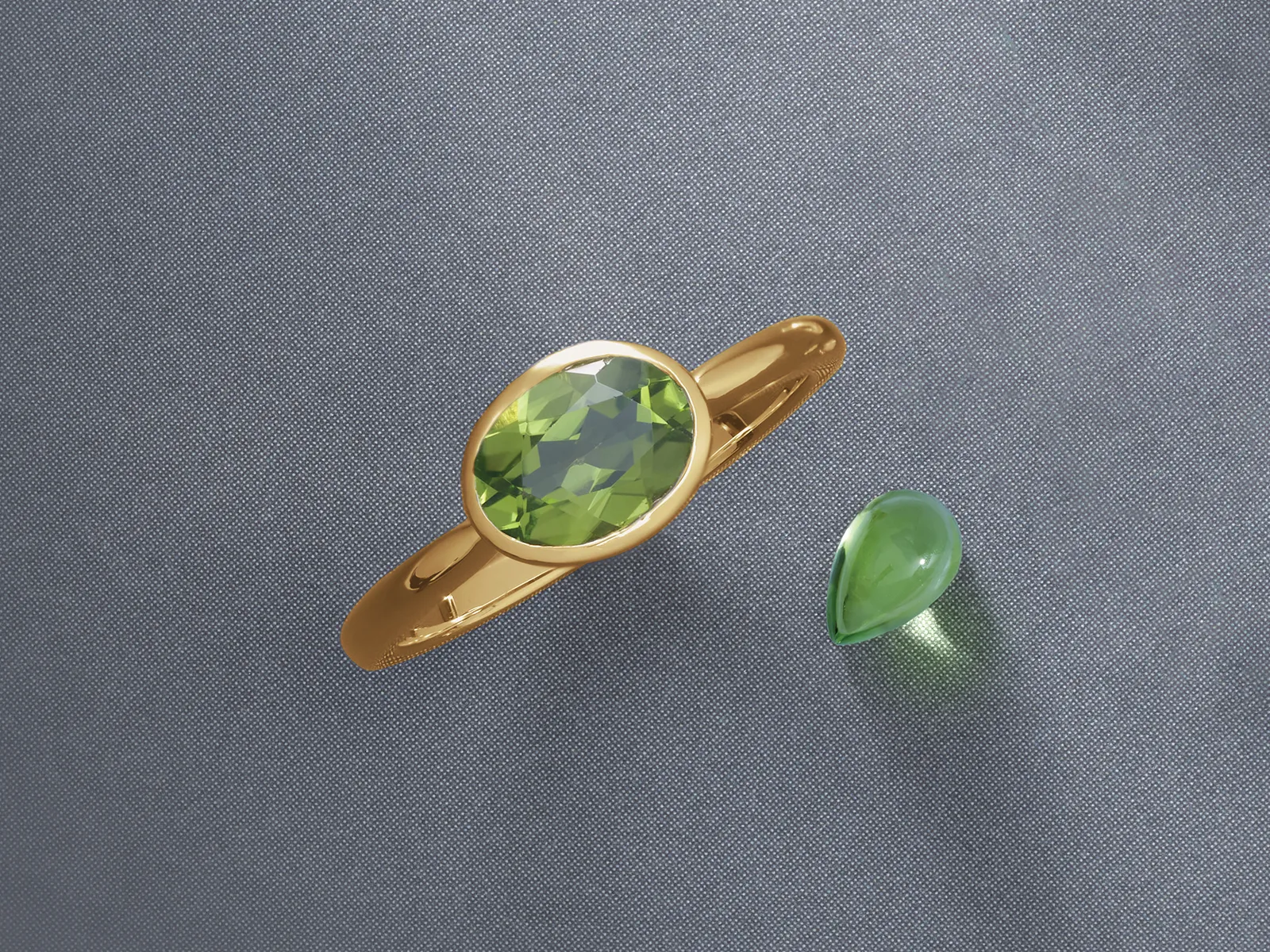 A gold ring with an oval green gemstone and a loose teardrop-shaped green gem on a gray background.