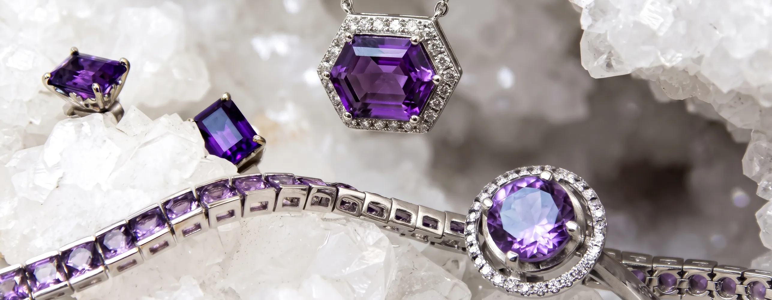Purple gemstone jewelry set on white crystals, featuring rings, a necklace, and a bracelet.