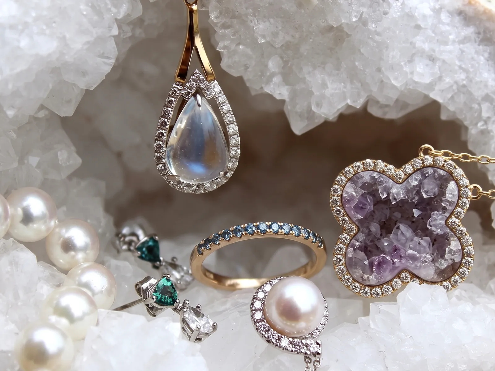 A collection of gemstone jewelry including a pearl necklace, emerald earrings, and a moonstone pendant on a crystal background.