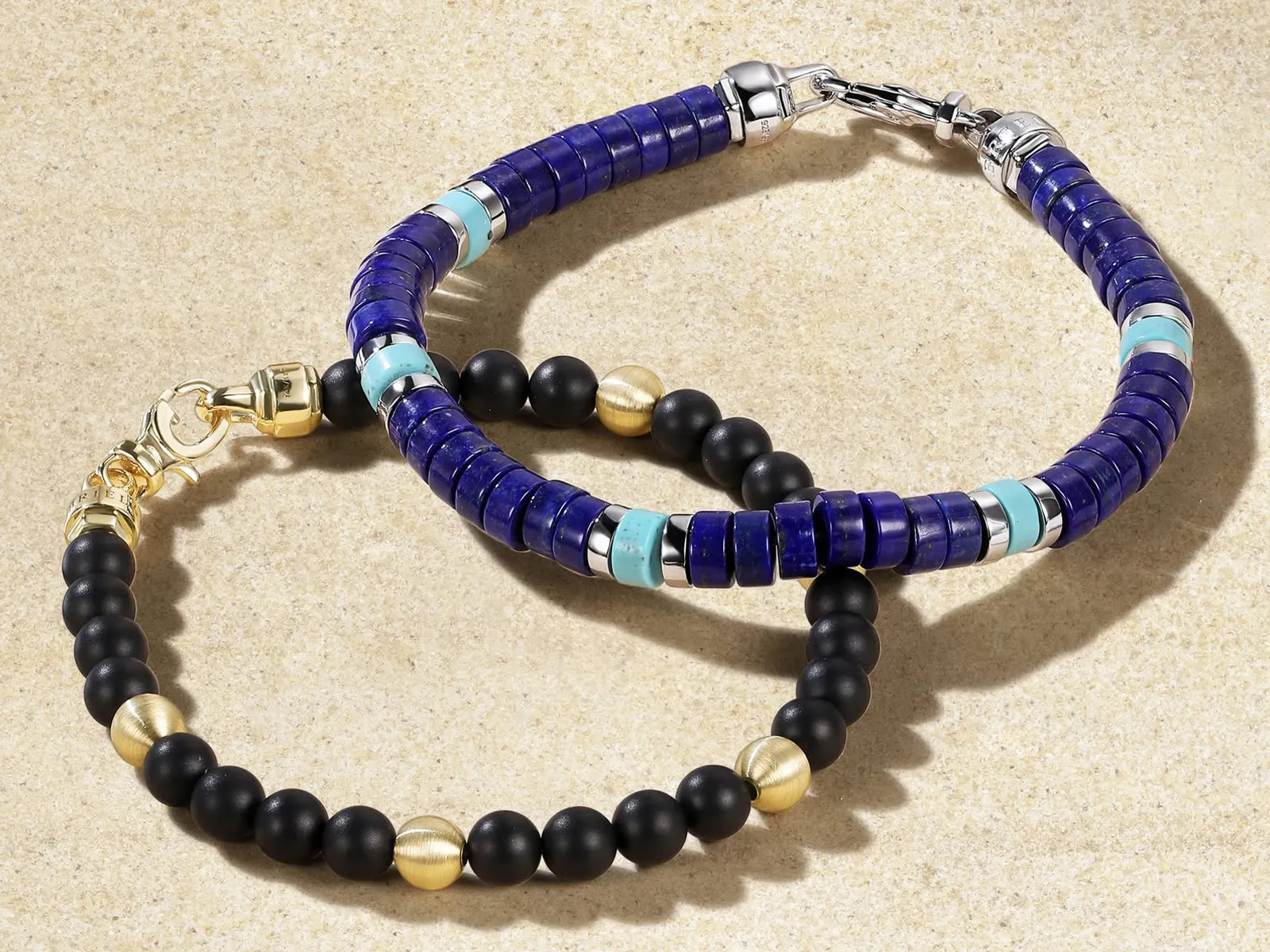 Two gemstone bracelets: one with blue and turquoise beads, the other with black and gold beads, on a textured surface.