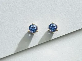 A hand wearing a gold ring with a blue oval gemstone surrounded by small diamonds.
