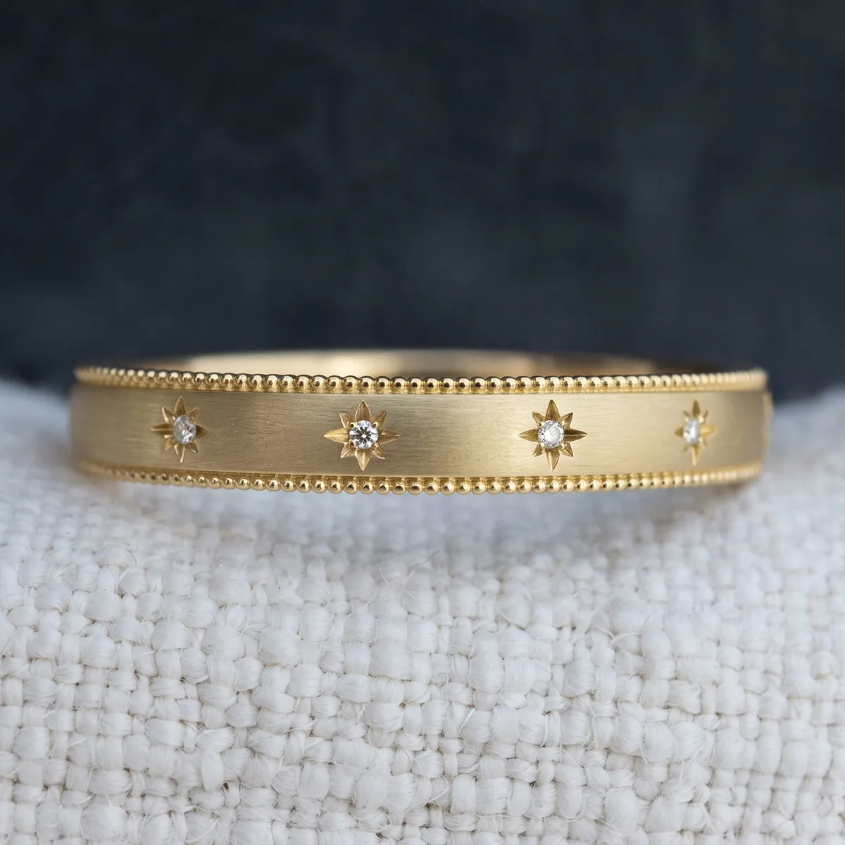 A gold bracelet with star-shaped diamond accents and beaded edges on a textured surface.