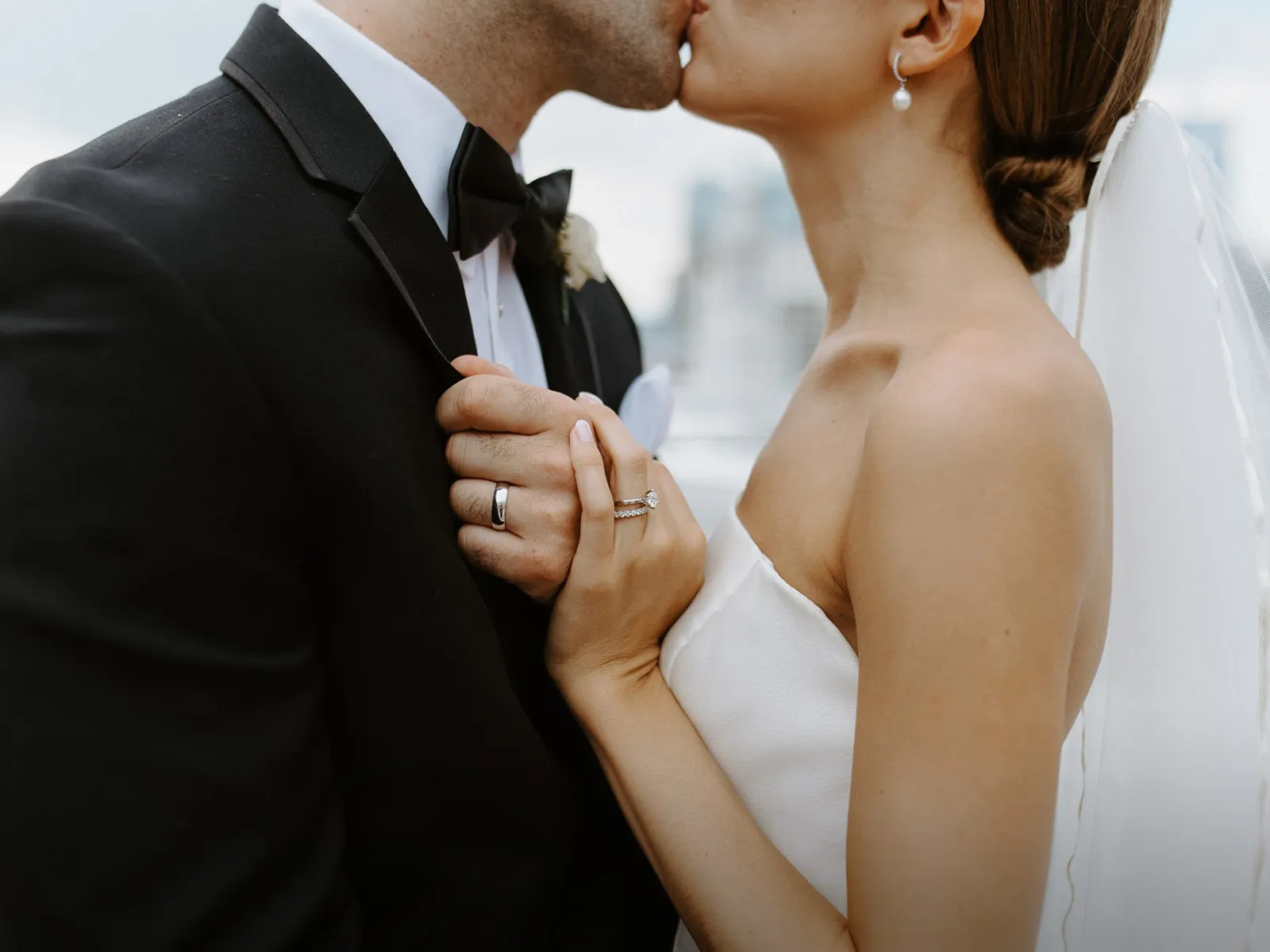 A bride and groom kissing, holding hands, showing wedding rings.