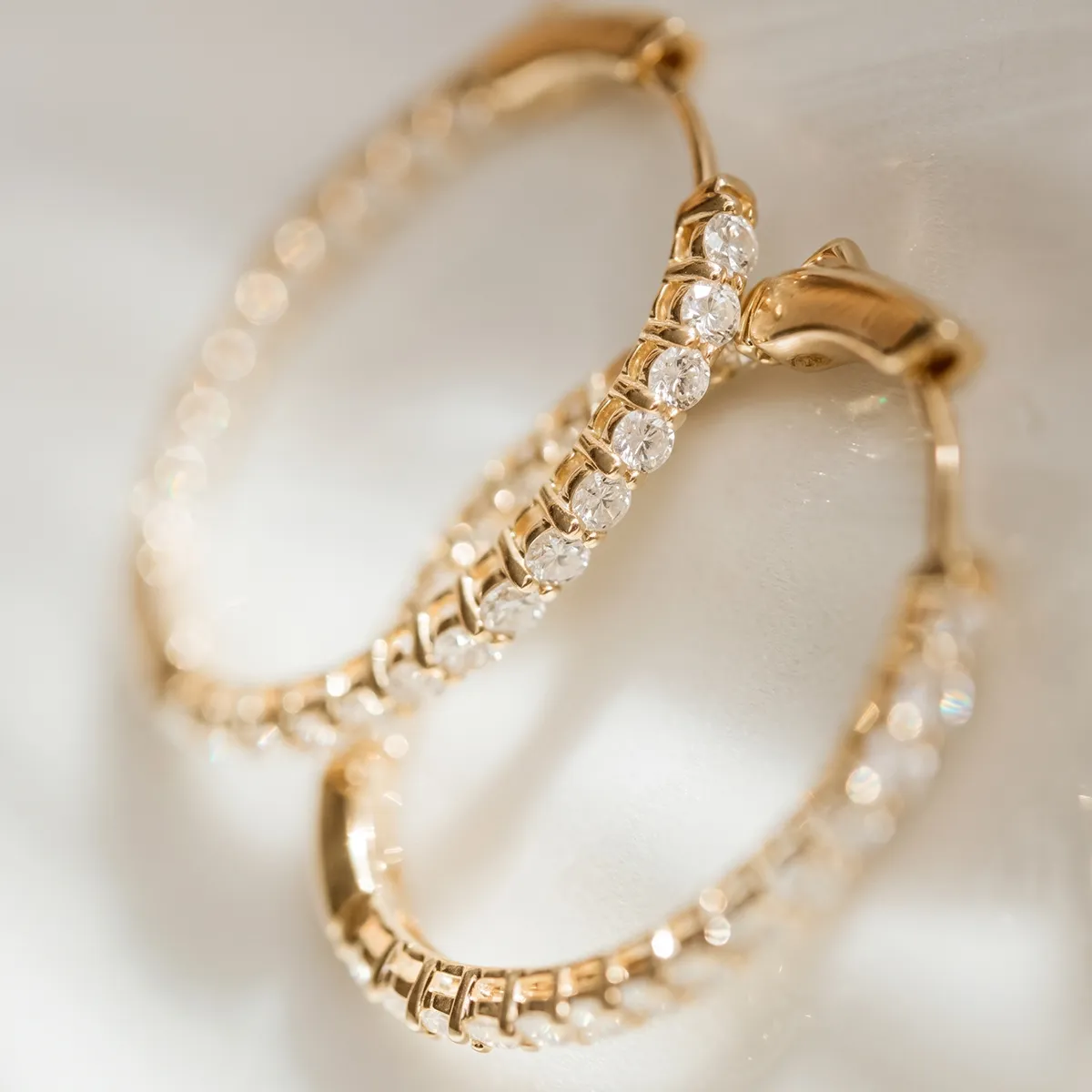 Gold hoop earrings adorned with sparkling diamonds on a light background.