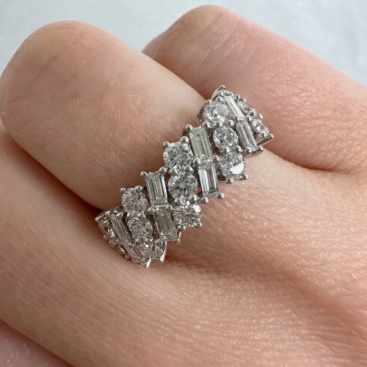 A hand wearing a diamond ring with round and baguette stones.