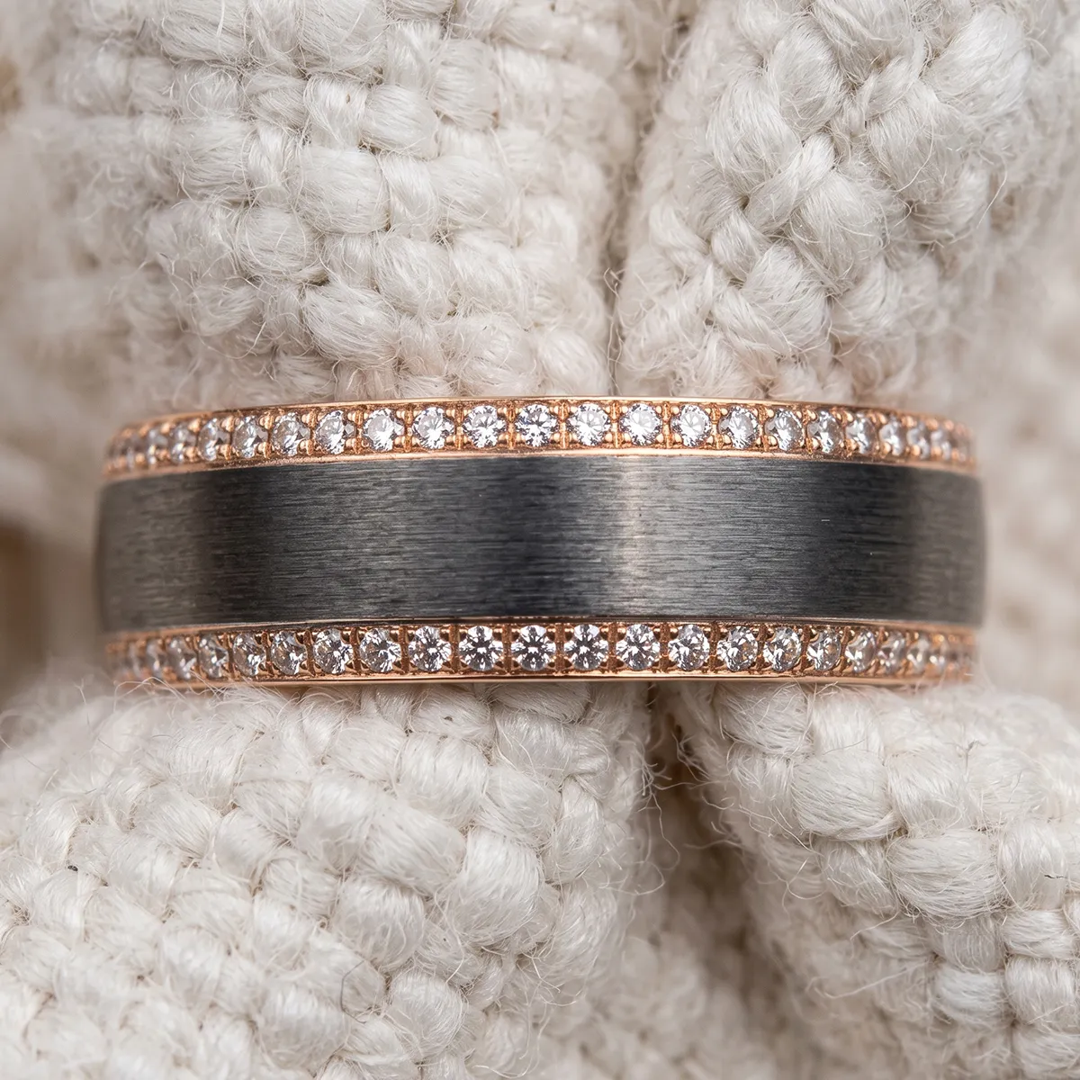 A diamond-studded ring with a brushed metal center on a textured white fabric background.