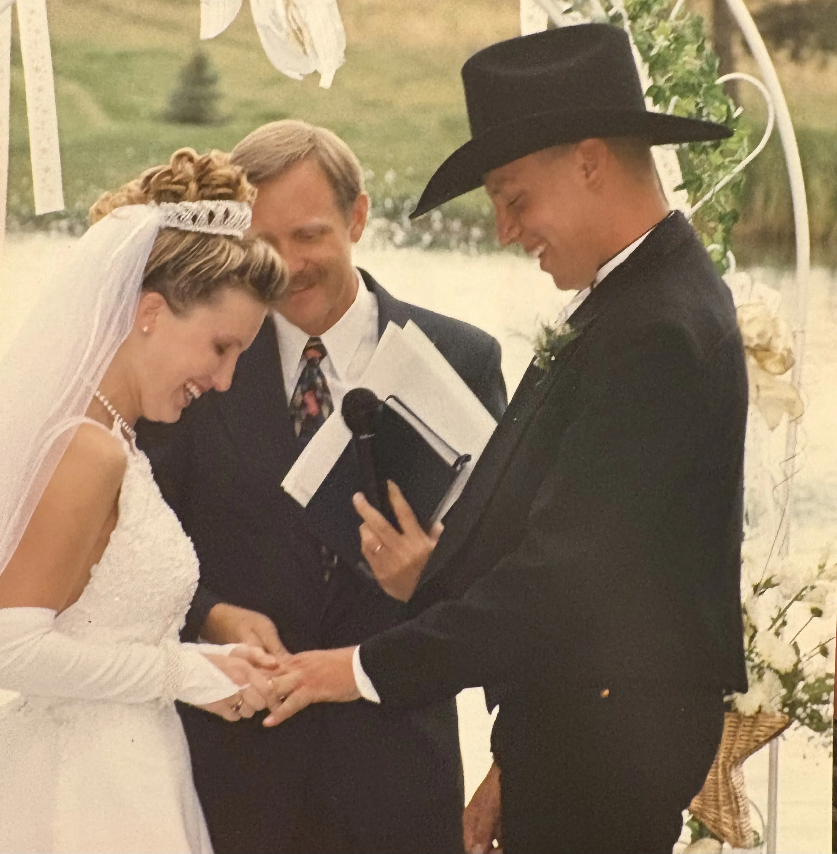 A couple smiling by a lake, woman showing engagement ring.