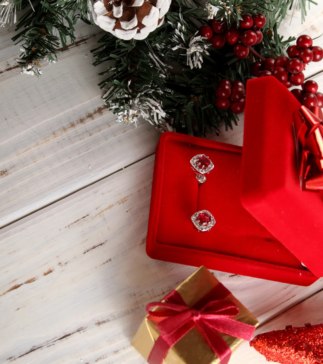 Red gemstone earrings in a red velvet box, surrounded by holiday decorations.