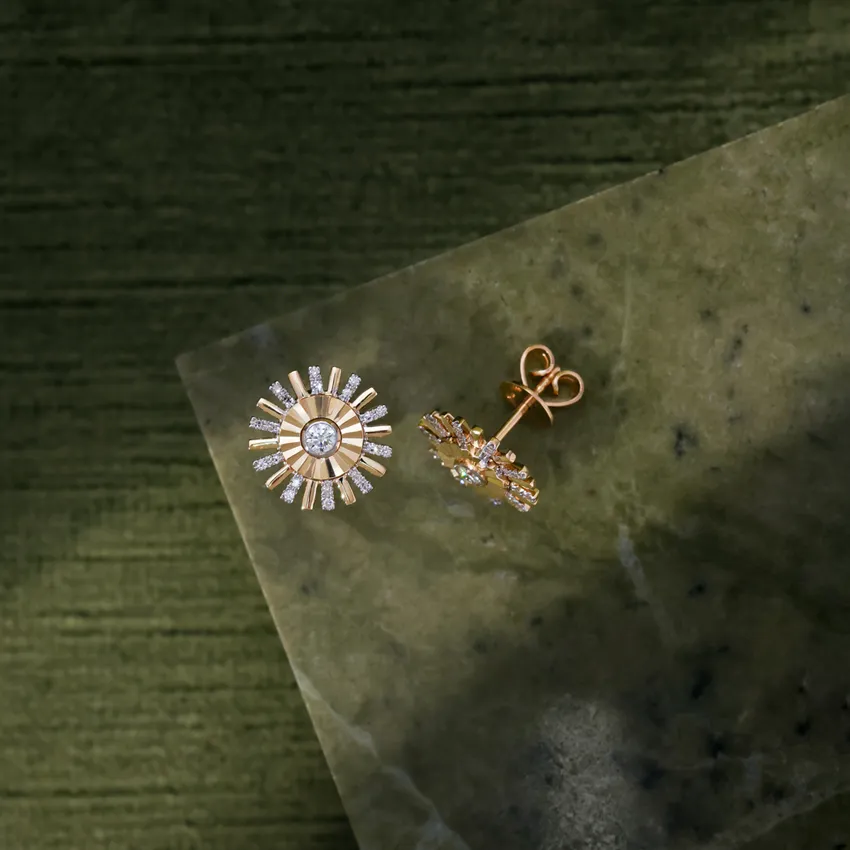 Gold sunburst earrings with sparkling stones on a green marble background.