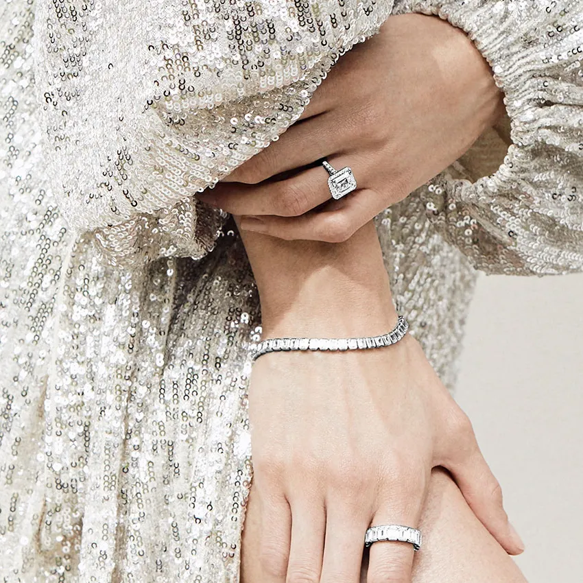 Elegant hands adorned with a diamond ring and tennis bracelet, wearing a sparkling sequined dress.