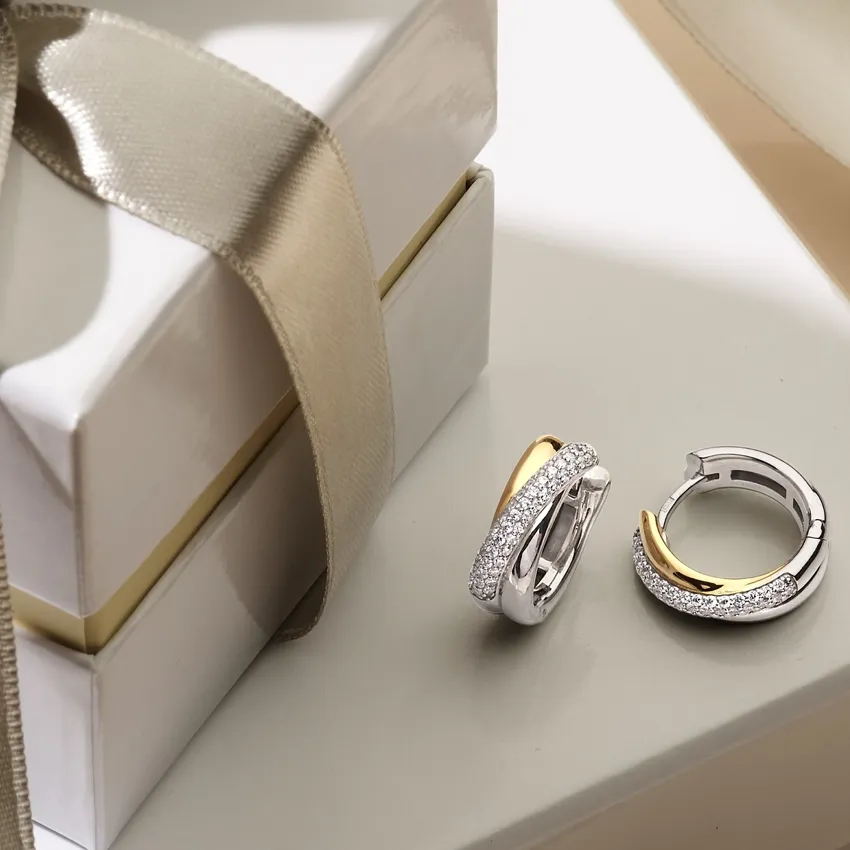 Elegant silver and gold hoop earrings beside a gift box with a ribbon.