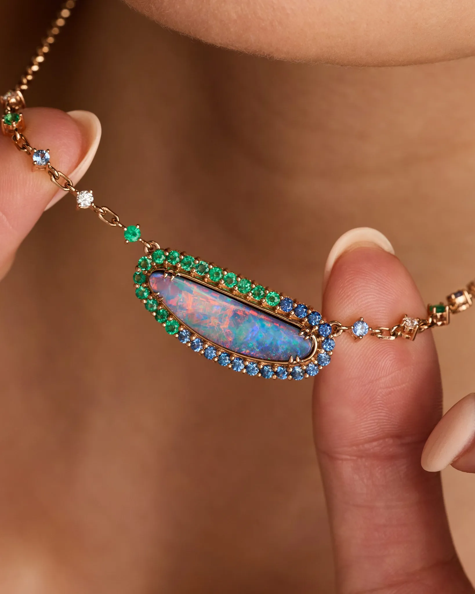 Close-up of a necklace with a colorful opal pendant surrounded by green and blue gemstones.
