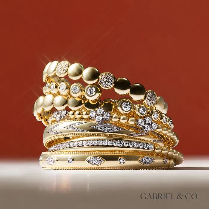 Luxurious gold and diamond bracelets draped over a satin fabric backdrop.
