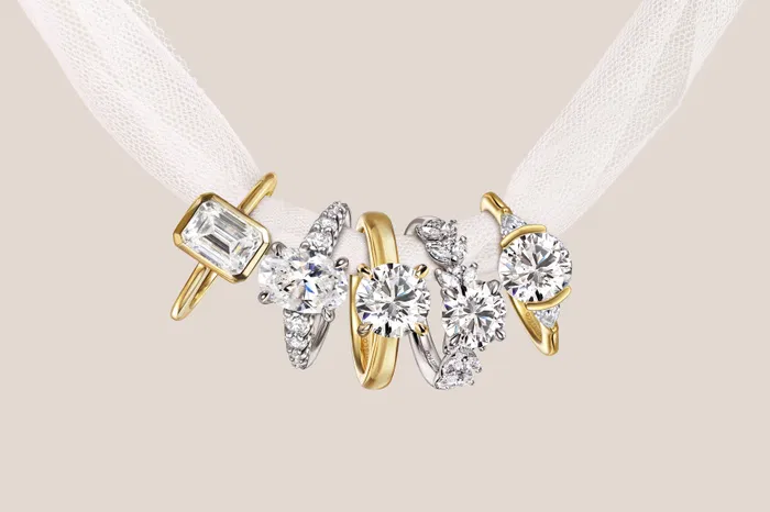 Two gold rings with large emerald-cut diamonds on a reflective surface.