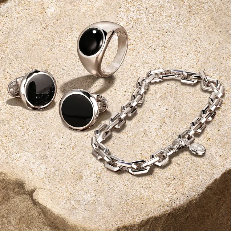 Men's silver rings and bracelet with black stones on a textured surface.