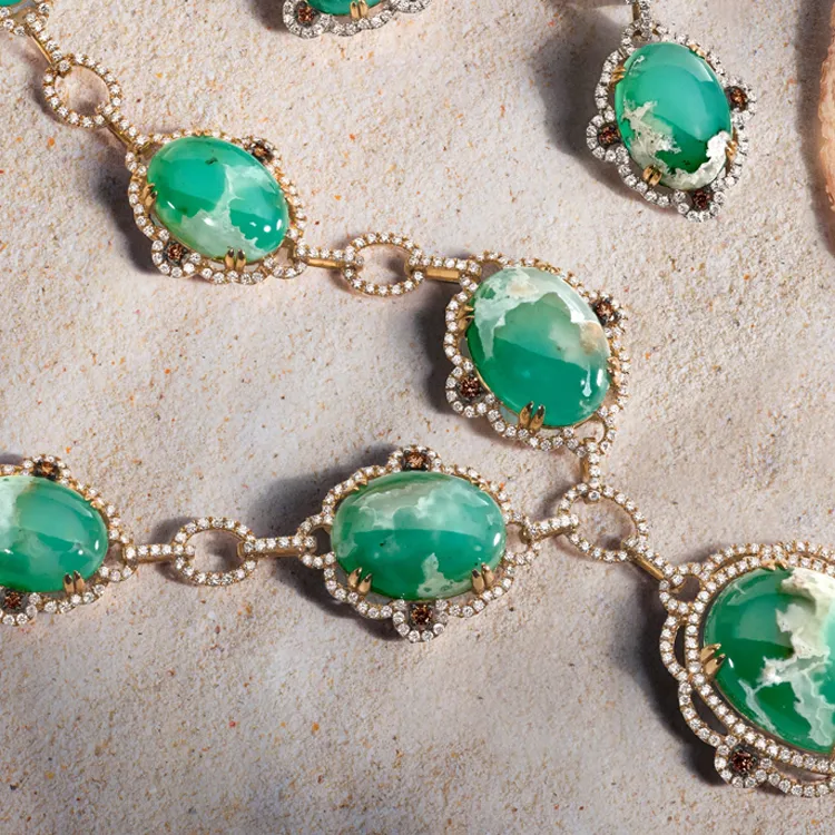Green gemstone necklace with diamond accents on a textured surface.
