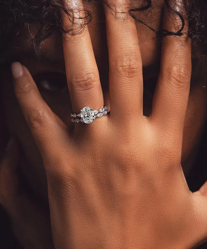 Close-up of a hand with a diamond engagement ring, partially covering the face.