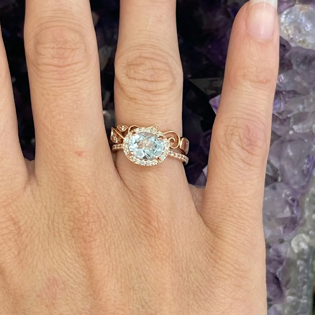 A hand wearing a rose gold ring with a large oval gemstone and diamond accents.