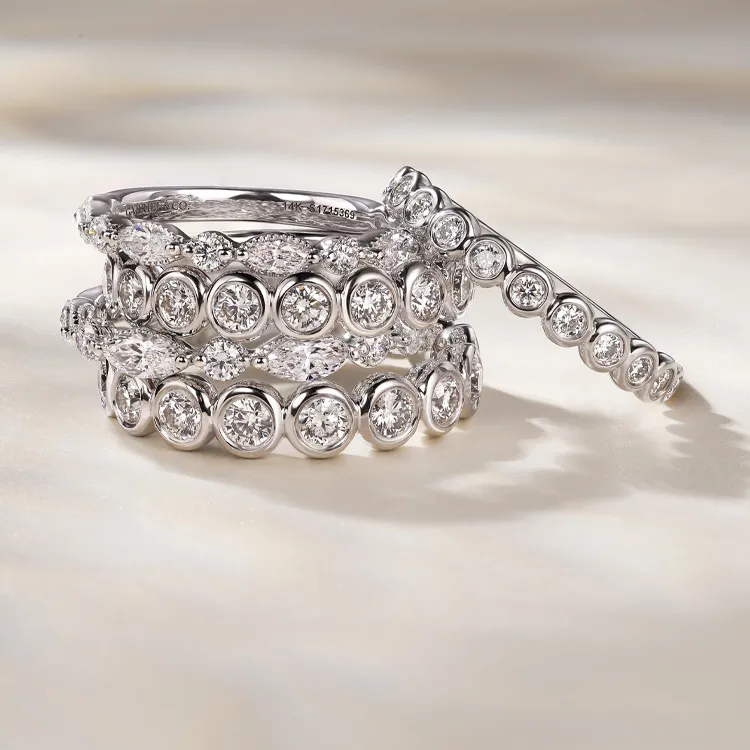 Stacked diamond rings with bezel settings on a light surface.