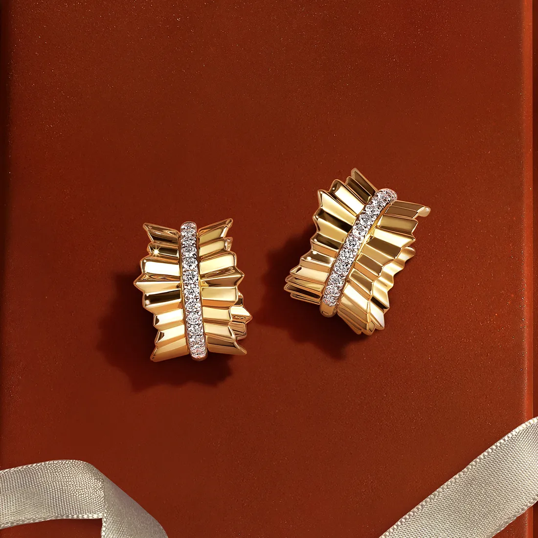 Gold earrings with diamond accents on a red background.