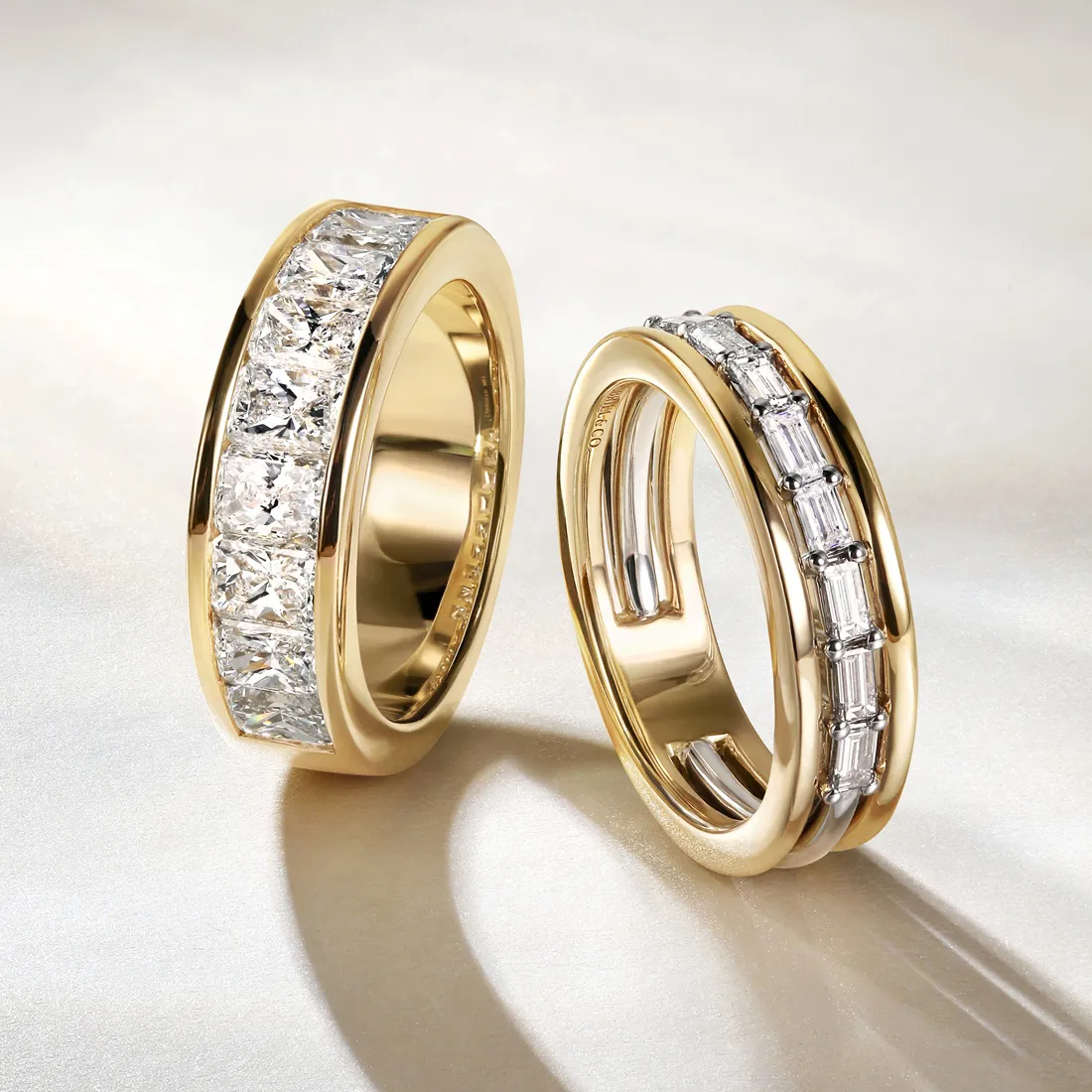 Two gold men's bands with embedded diamonds on a light background.