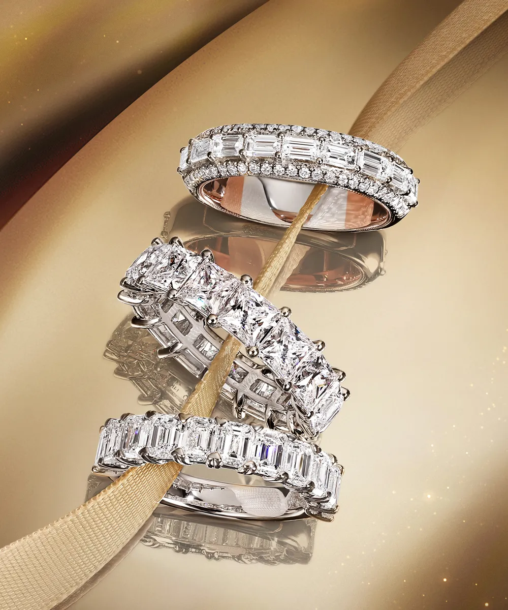 Three diamond eternity bands on a reflective surface with a gold ribbon.