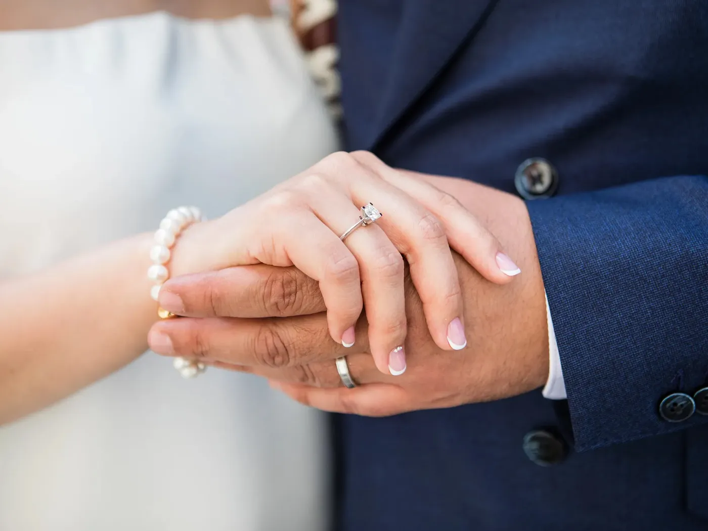 Close-up of couple's hands with engagement ring and pearl bracelet.