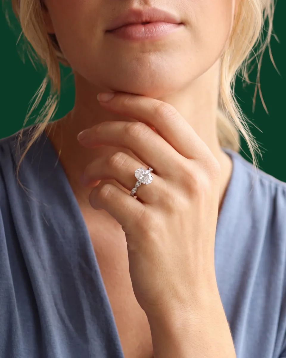 Pear-shaped diamond ring with halo setting on a finger, green background.