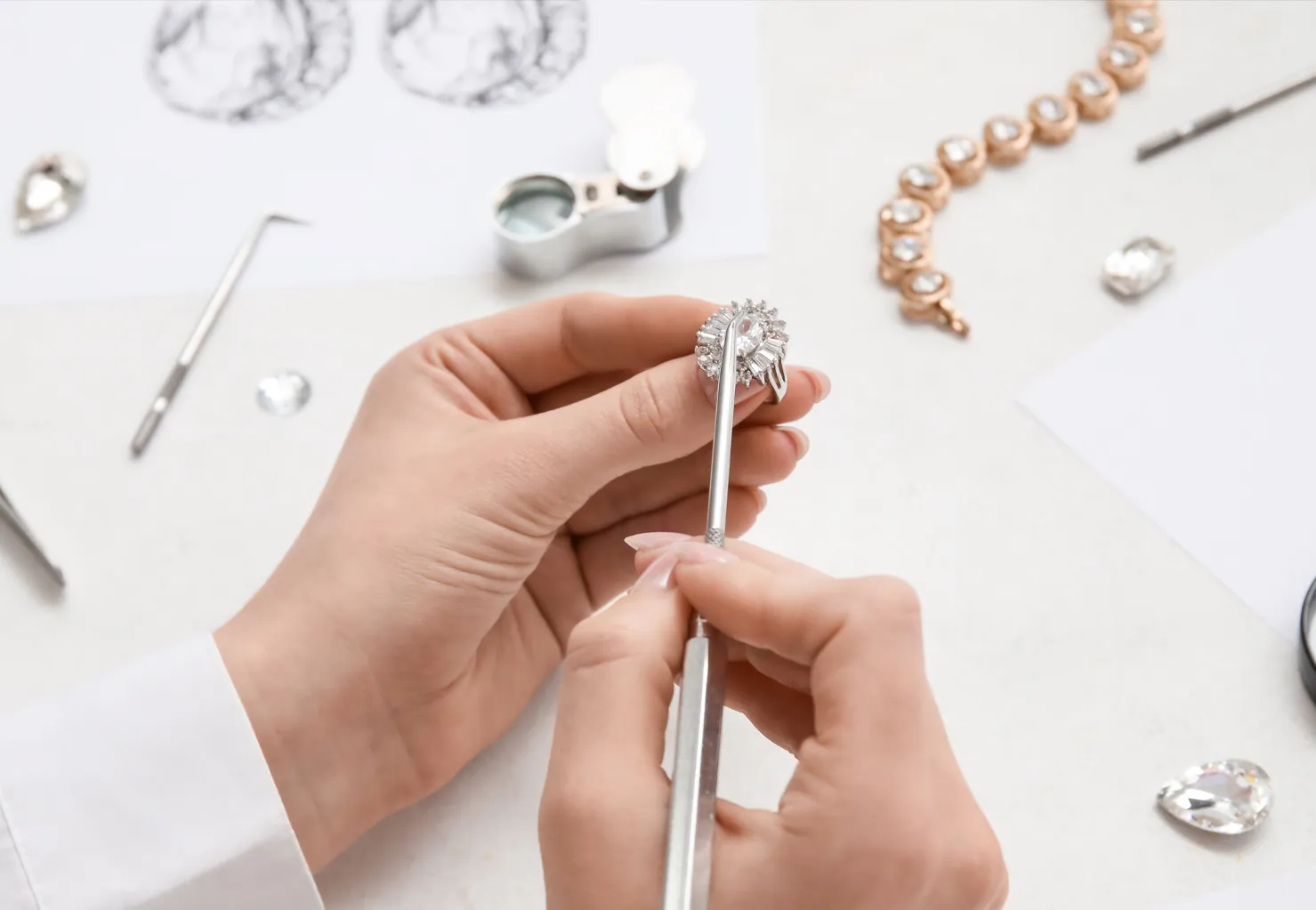 Jeweler working on a diamond ring with tools and sketches on a table