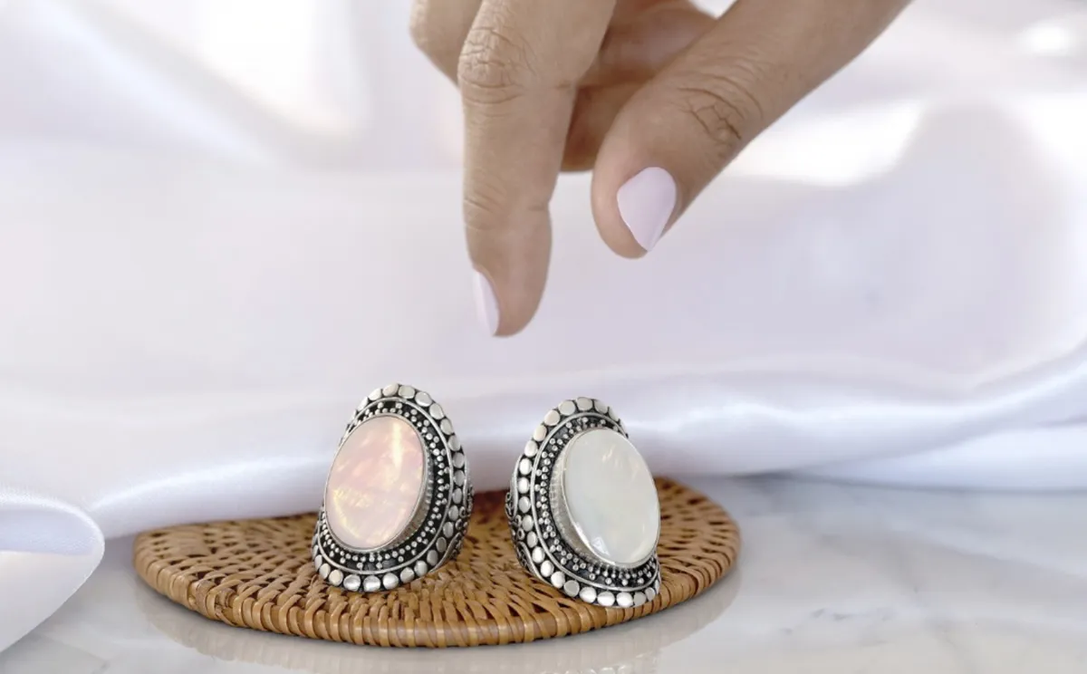 A hand reaching for two decorative rings on a woven tray, showcasing their unique designs and colors.