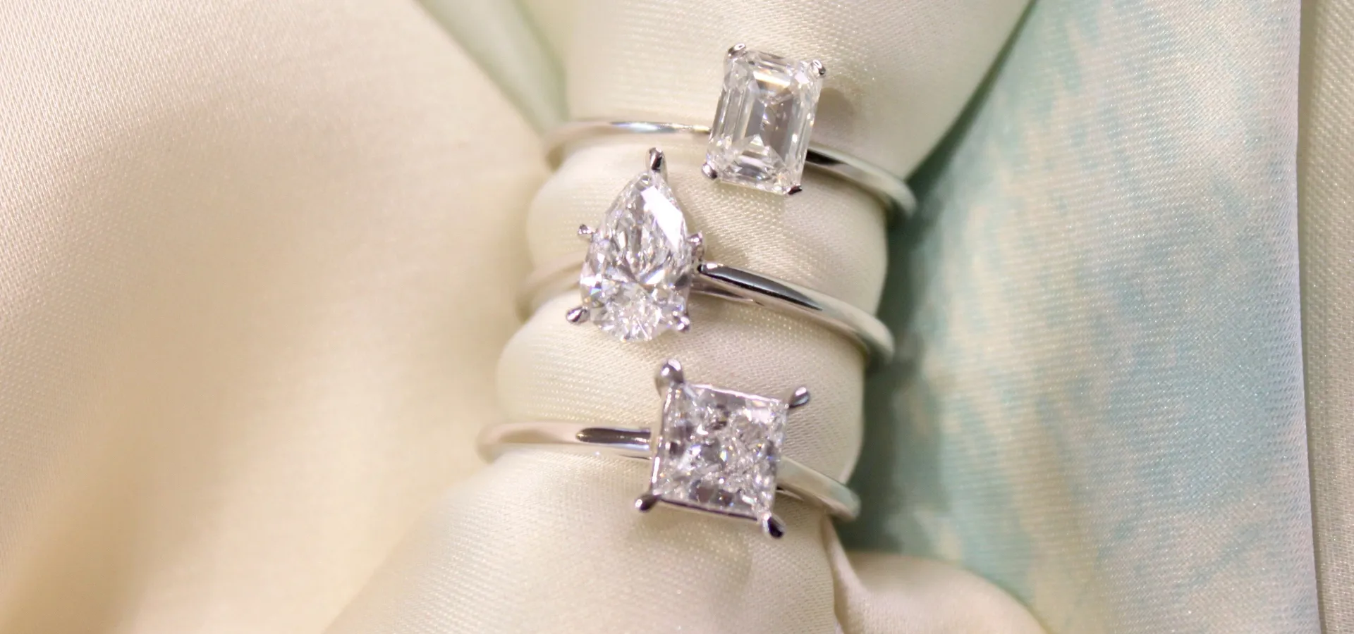 Three elegant engagement rings displayed on a soft fabric background. 