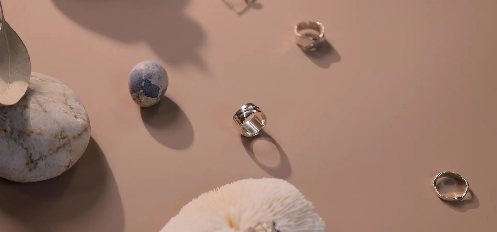 Silver rings and decorative stones arranged on a beige surface.