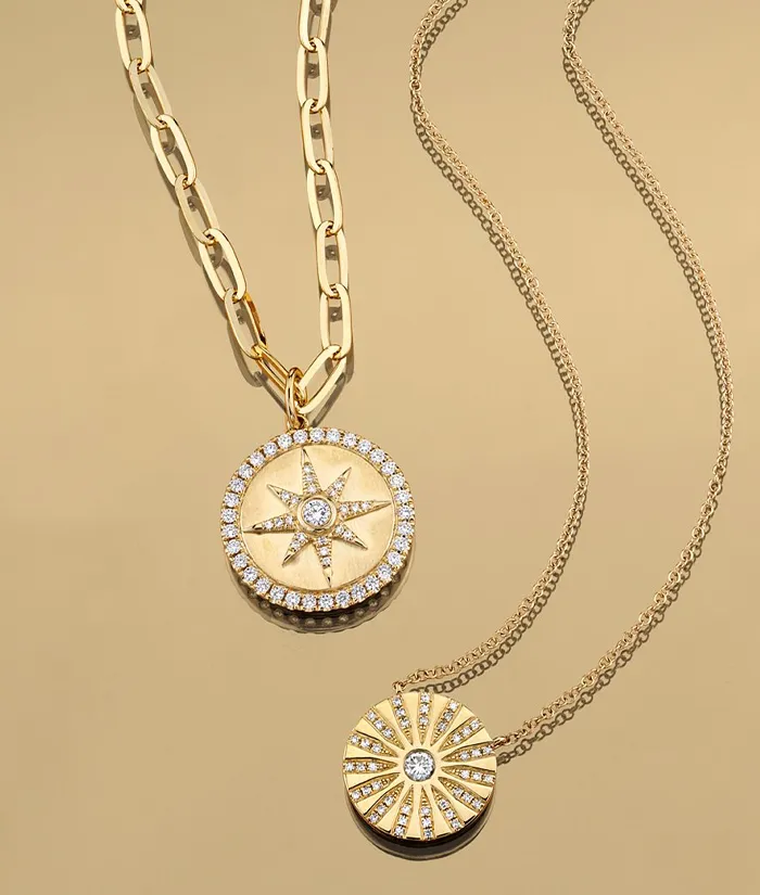 Gold compass pendant necklace with diamonds on a gold chain, displayed on a beige background. Shop at Bryan Jewelry in Prattvill