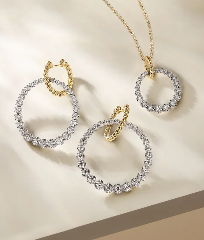 Three elegant jewelry pieces: two diamond hoop earrings and a diamond pendant on a soft background.