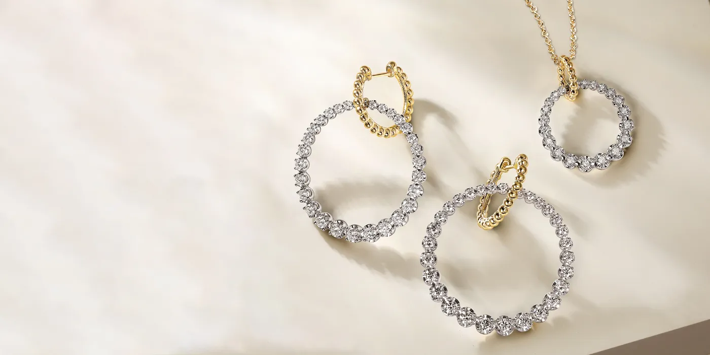 Three elegant jewelry pieces: two diamond hoop earrings and a diamond pendant on a soft background.