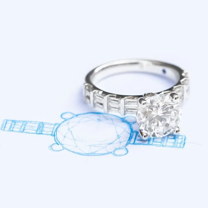 Diamond engagement ring beside its design sketch on a light background. Visit Bryan Jewelry in Prattville for more.