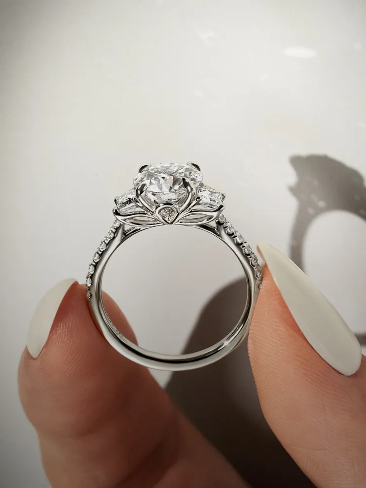 Elegant diamond engagement ring held between fingers, showcasing intricate design. Shop now at Bryan Jewelry in Prattville.