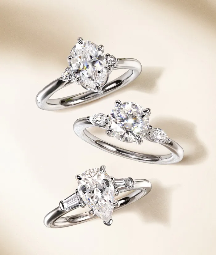 Three elegant diamond engagement rings displayed on a soft background, showcasing various styles and settings.