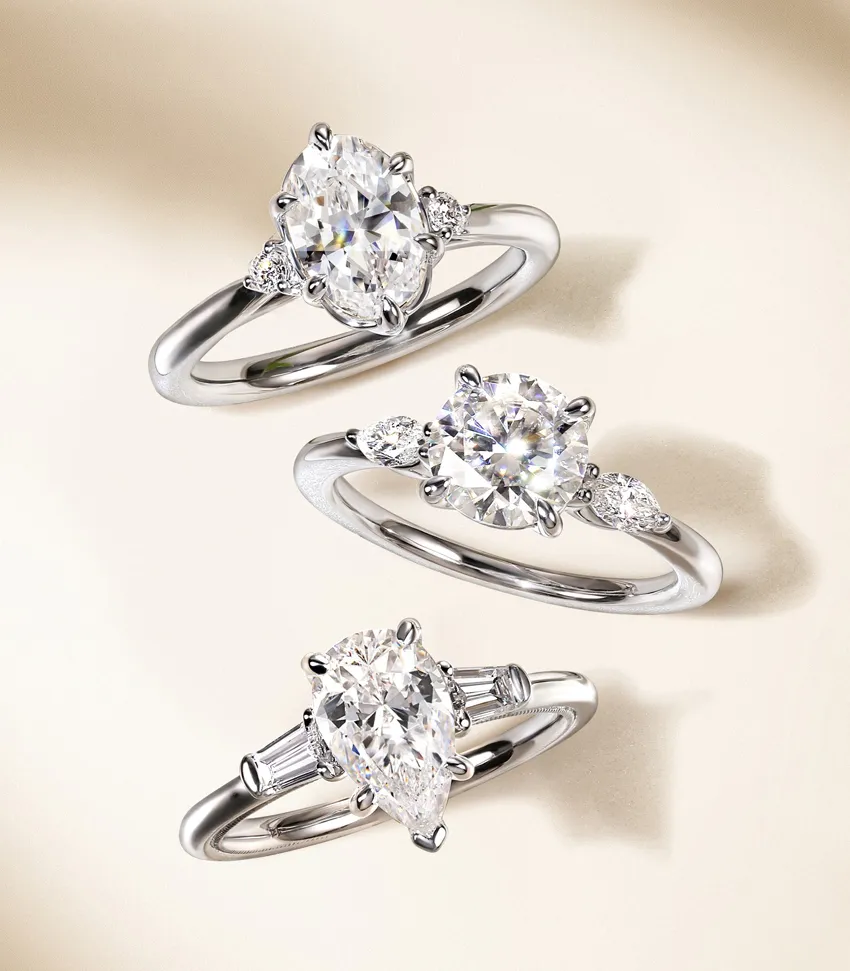 Three elegant diamond engagement rings displayed on a soft background, showcasing various styles and settings.