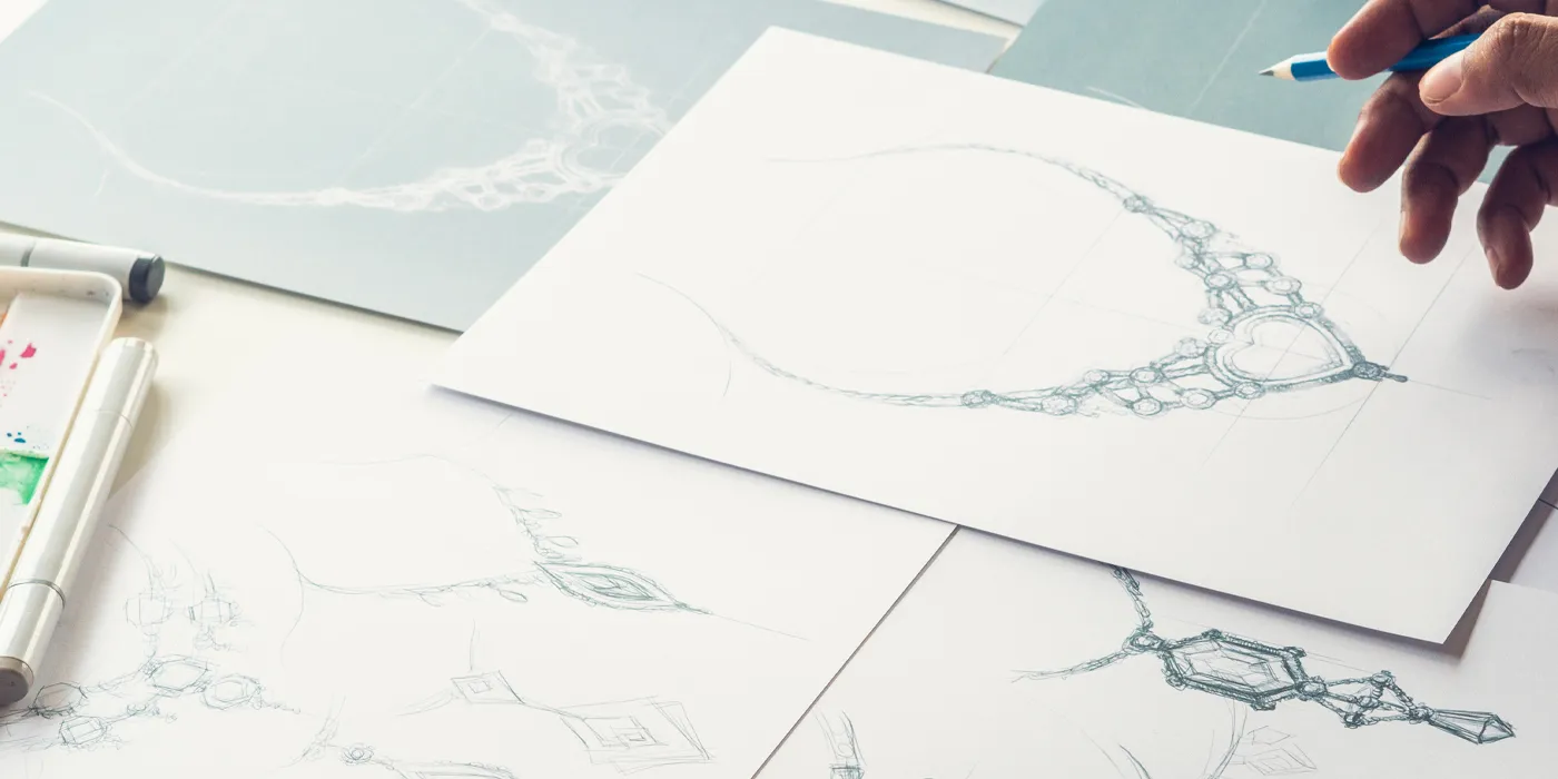 Hand sketching of intricate jewelry designs on paper, with colored markers and a pencil in use.
