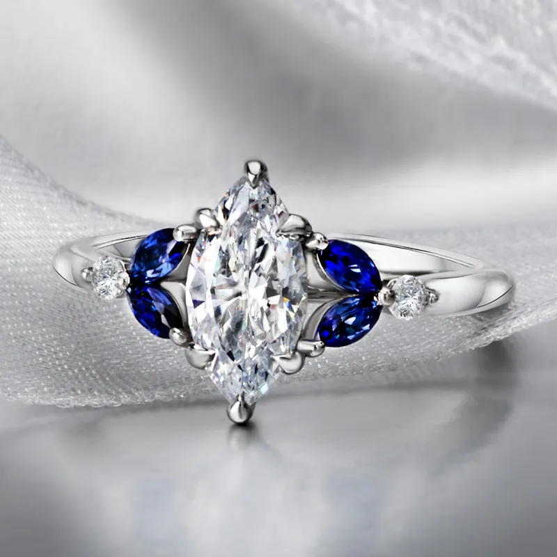 Elegant marquise diamond ring with blue sapphires and smaller diamonds, perfect for engagement. Visit Bryan Jewelry.