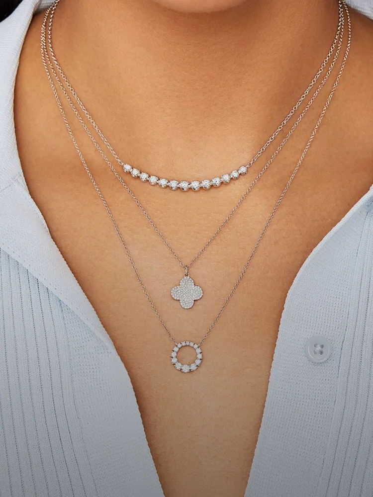 Three layered diamond necklaces featuring a floral pendant, a circular pendant, and a diamond bar, worn on a model.