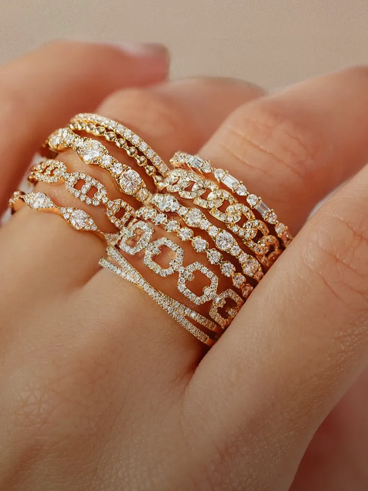 A hand displaying multiple gold diamond rings stacked together. Visit Bryan Jewelry for more fine jewelry options.