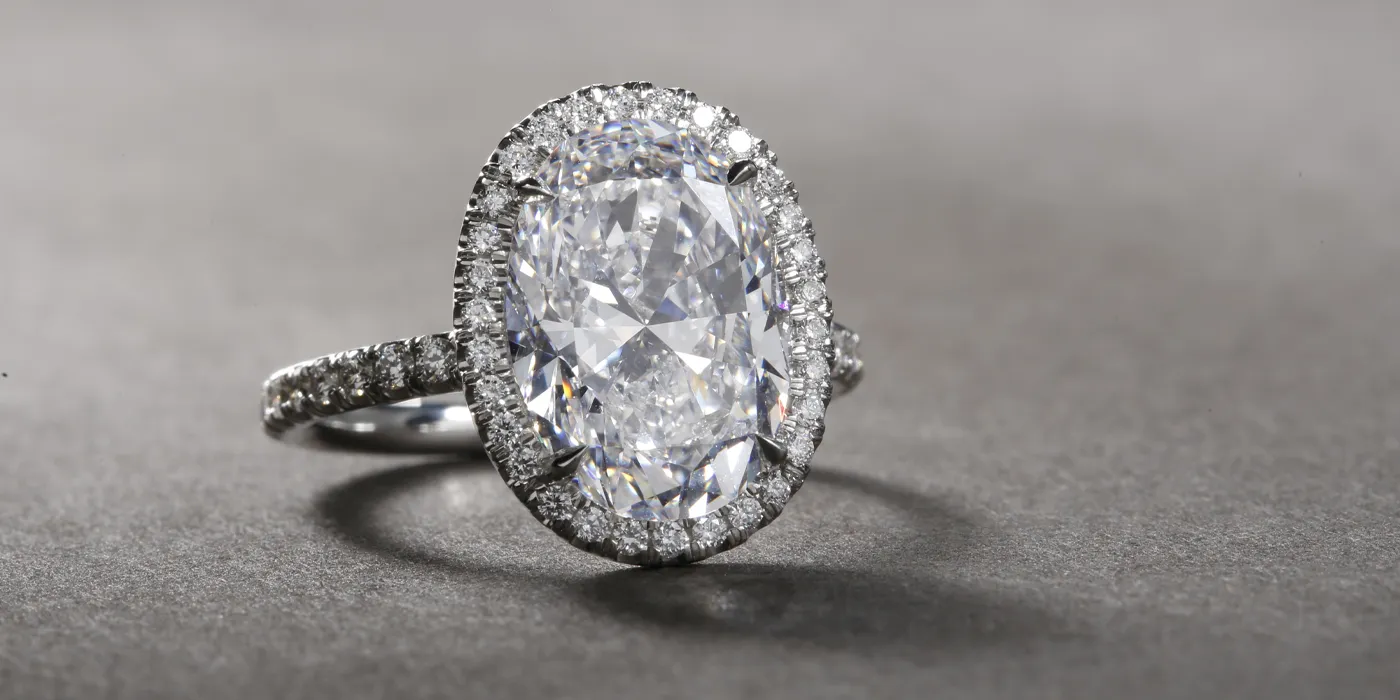 Elegant oval diamond engagement ring with a halo of smaller diamonds, set on a delicate band. Visit Bryan Jewelry in Prattville.