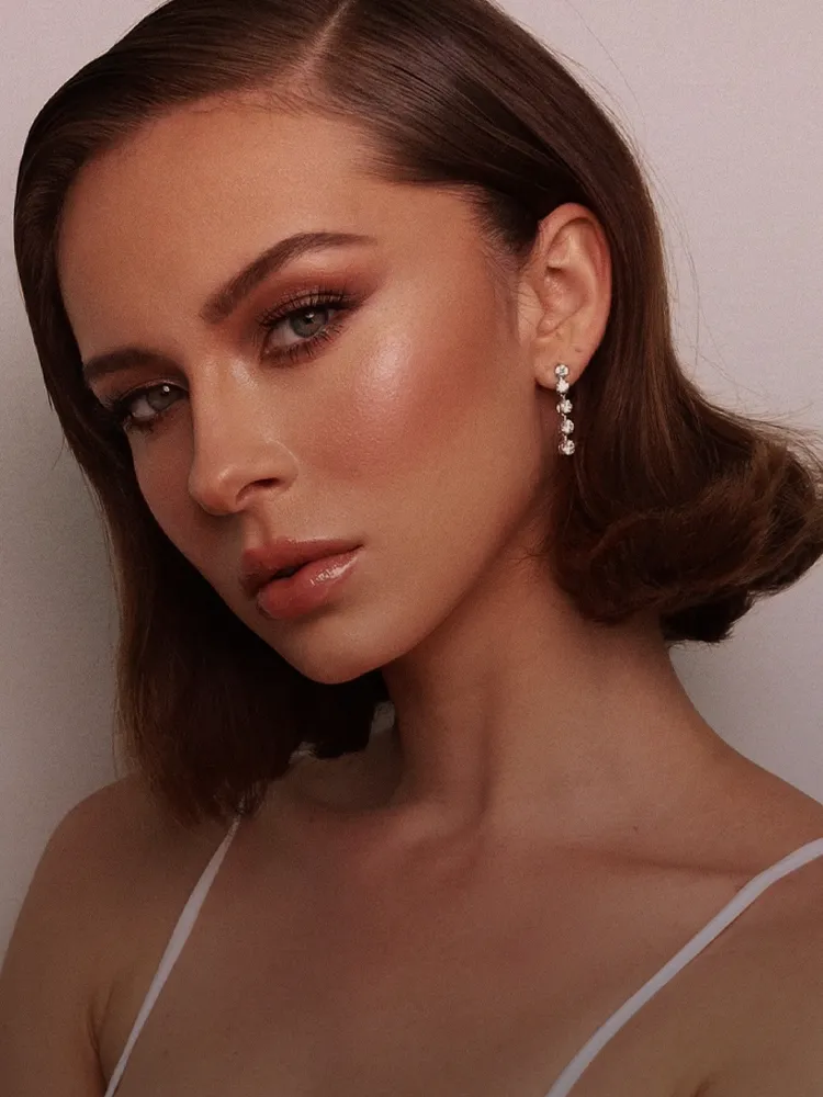 Elegant woman with makeup and earrings, promoting Bryan Jewelry's earrings collection. 
