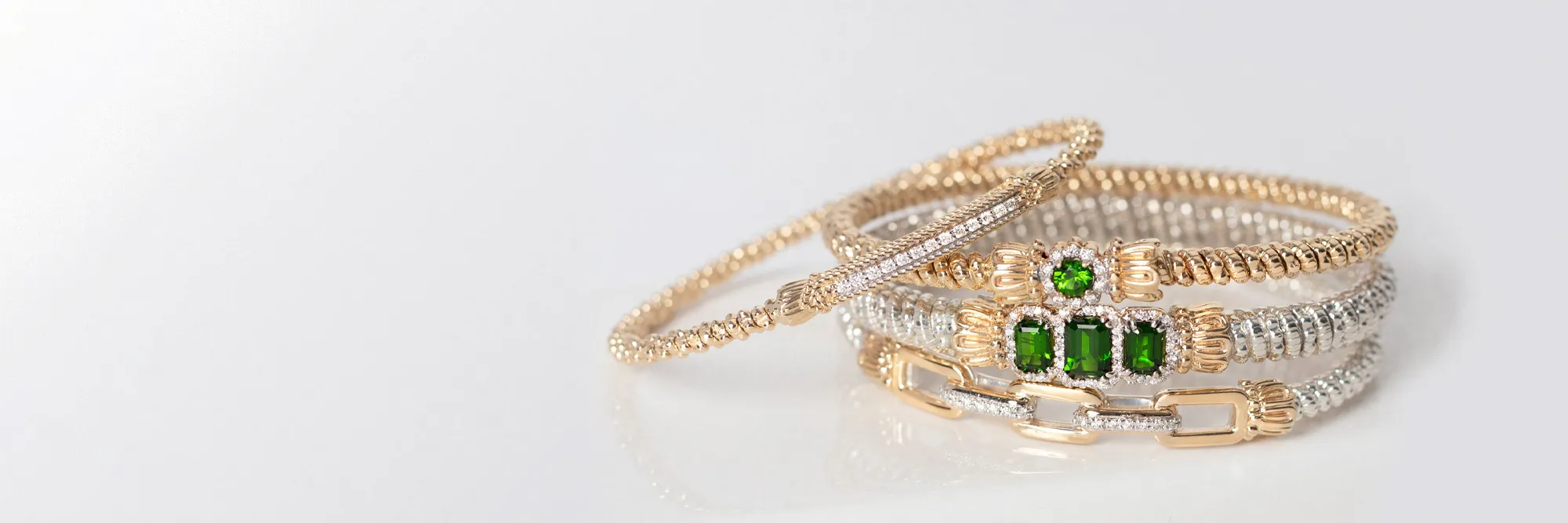 Three elegant bracelets featuring gold and silver designs with green gemstones, promoting birthstone jewelry.