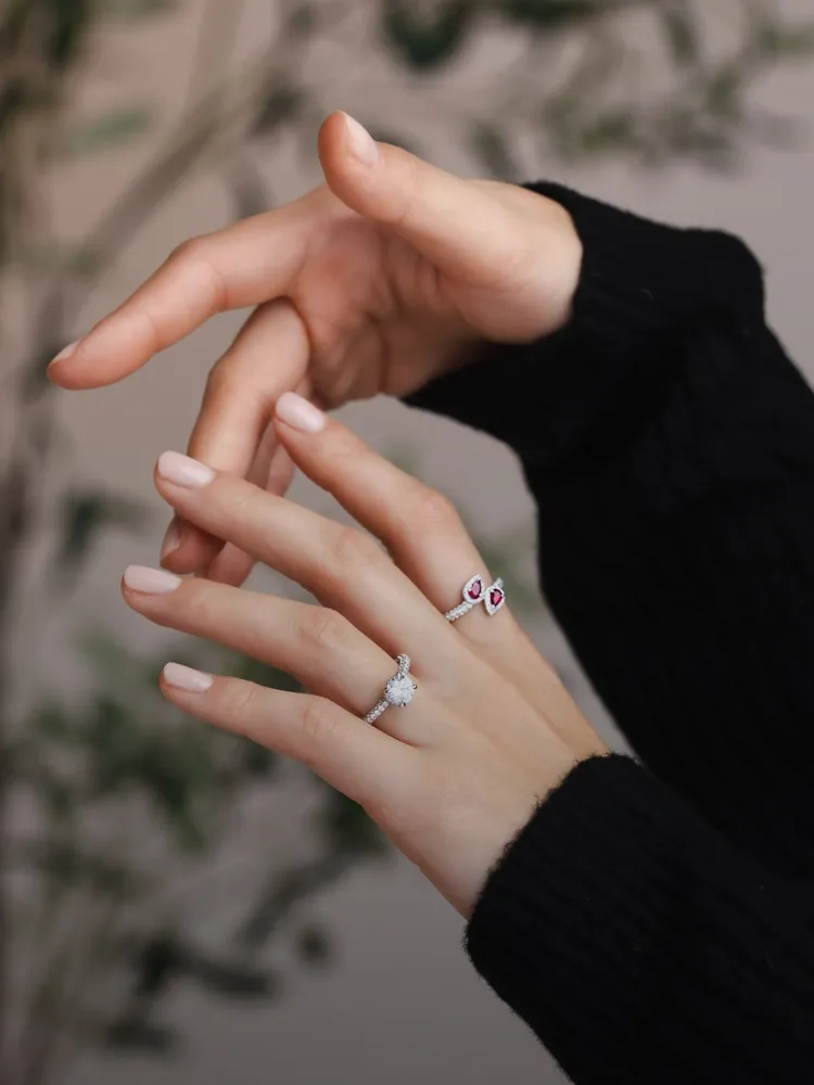 Elegant hands showcasing a diamond engagement ring and a stylish ring with red accents. Shop Engagement Rings at Bryan Jewelry.